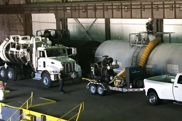 A technician monitors vapor levels near the tank car's top manway cover while the inside of the tank car is being cleaned