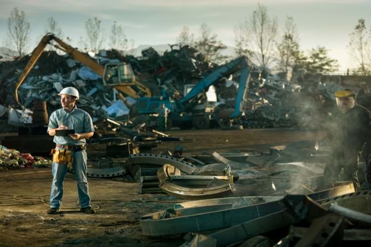 Caucasian engineer standing at scrap metal recycling site, inspecting work