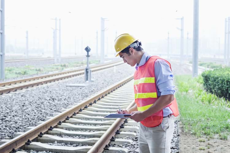 A railroad worker in protective work gear checking the railroad tracks