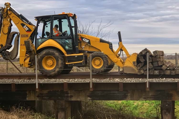 A railroad worker driving a back loader, pushing railroad ties on top of the railroad track