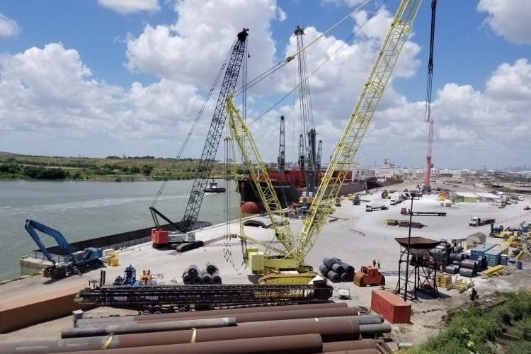 Transloading cranes transferring metal pipes and sheet rolls at a busy port