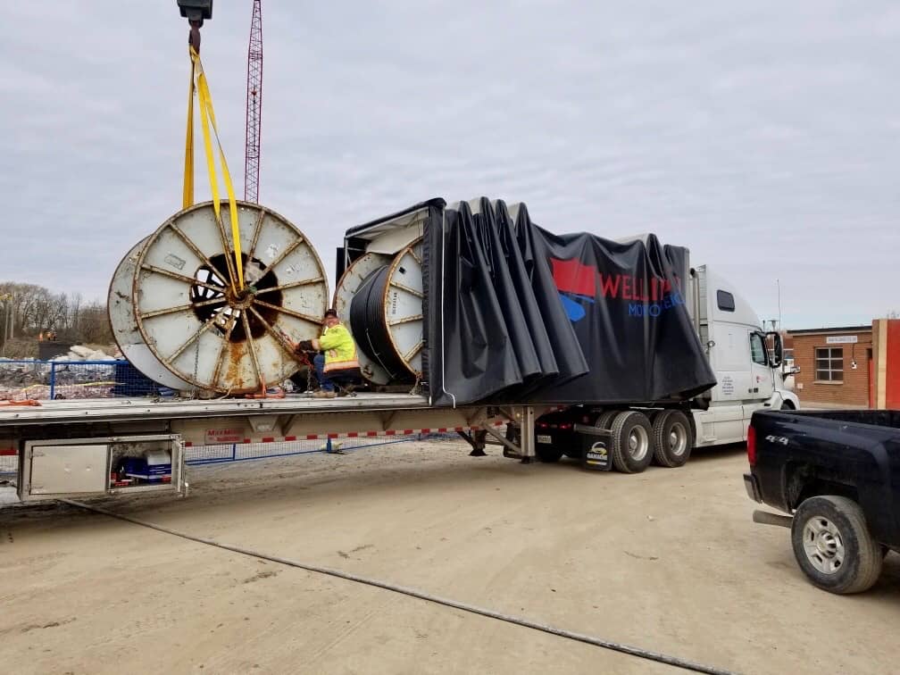 A Wellington Motor Freight rolltite is being loaded with large spools of industrial material as part of a larger project. The driver is assisting with the product being loaded.