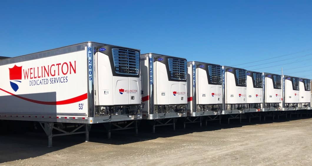 A lineup of clean and shinny, Wellington Dedicated Services refrigerated trailers parked in the company yard.