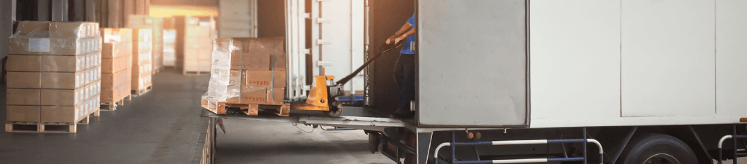 A standard palette of goods being moved off of a transport truck with a liftgate onto a loading dock. An employee is using a pump truck to move the skid.